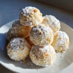 A pile of melt-in-mouth snowball cookies dusted with powdered sugar and sprinkled with chopped nuts.