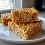 A stack of three perfectly square, soft Rice Krispie treats glistening with melted marshmallow.