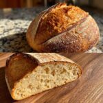 A golden-brown, crusty sourdough bread loaf and a slice revealing its airy crumb structure.