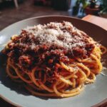 A close-up of a plate of Spaghetti Bolognese, topped with rich meat sauce and grated Parmesan cheese.