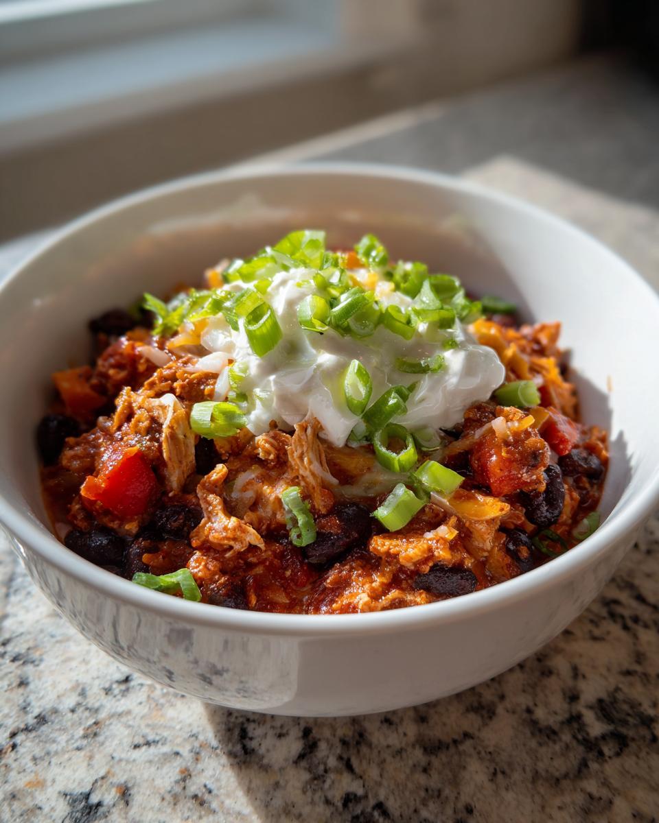 A close-up of a hearty bowl of Turkey chili topped with a dollop of sour cream and fresh sliced green onions.