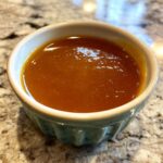 A close-up of a small blue ramekin filled with smooth, rich turkey gravy.