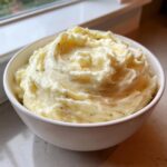 A white bowl filled with creamy, fluffy garlic mashed potatoes, showing swirls and melted butter.