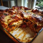 A close-up, angled view of a freshly baked vegetable lasagna in a glass baking dish, with a slice removed.