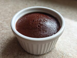 A close-up of rich, dark chocolate pudding set in a small, white, fluted ramekin.