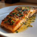 Close-up of a perfectly cooked baked salmon recipe fillet glazed with butter, garlic, and fresh parsley.