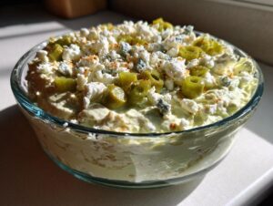 A creamy, pale green dirty martini dip topped with crumbled feta, blue cheese, sliced green olives, and paprika.