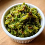 Close-up of chunky, bright green tomato salsa topped with dark, caramelized bits, served in a small white bowl.