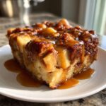 Close-up of a moist slice of apple bread pudding generously drizzled with rich caramel sauce.