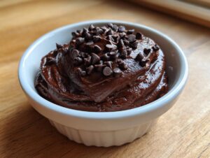 Close-up of rich, dark brownie batter dip served in a white ramekin and topped with mini chocolate chips.