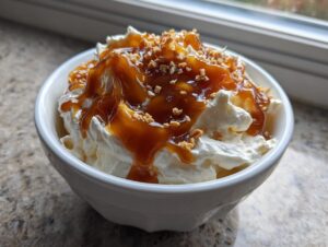 A rich, creamy apple dip topped with thick caramel sauce and chopped nuts, served in a white bowl.