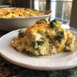 A serving of creamy chicken broccoli rice casserole topped with melted cheddar cheese on a white plate.