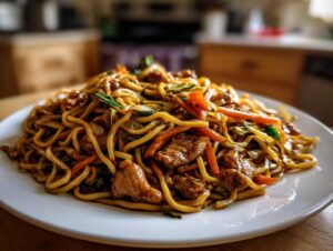 A close-up of a generous serving of savory chicken chow mein recipe, featuring noodles, chicken pieces, and stir-fried vegetables.