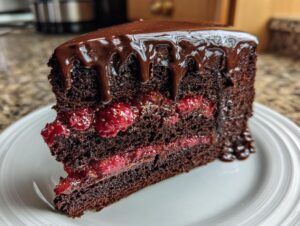 A decadent slice of chocolate raspberry cake featuring dark layers, bright raspberry filling, and dripping chocolate ganache.