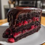 A rich slice of chocolate raspberry cake featuring dark layers, bright raspberry filling, and dripping chocolate ganache.