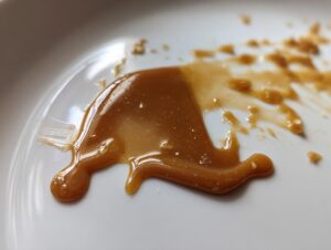 Macro shot of thick, glossy brown peanut sauce smeared on a white plate.