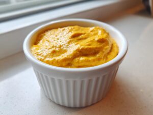 Close-up of vibrant orange cottage cheese queso dip served in a small, white, fluted ramekin.