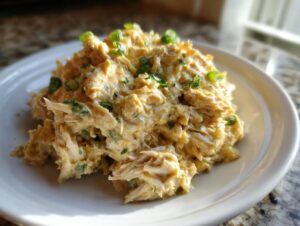 A close-up of shredded chicken mixed with a creamy sauce, resembling cream cheese chicken chili, topped with green onions.
