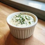 A white ramekin filled with creamy horseradish sauce, topped generously with chopped green chives.