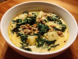 Close-up of a hearty bowl of creamy italian sausage soup featuring crumbled sausage, dark green kale, and white potato chunks.