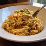 A fork lifts a creamy bite of chicken and orzo pasta from a white bowl of lemon chicken orzo.