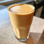 A close-up of a thick, creamy peanut butter banana smoothie served in a tall, faceted glass.
