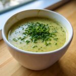 A close-up of creamy zucchini soup in a white bowl, garnished generously with chopped fresh chives.
