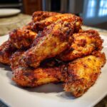 A close-up stack of golden brown, seasoned, crispy air fryer chicken wings piled high on a white plate.