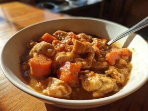 Close-up of a white bowl filled with rich slow cooker chicken stew featuring chunks of chicken and carrots.