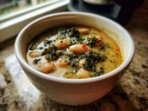 Close-up of a white bowl filled with creamy tuscan white bean soup featuring cannellini beans and dark leafy greens.