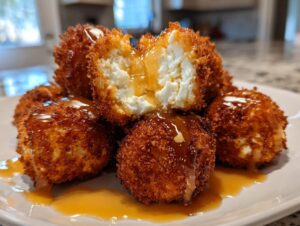 Close-up of crispy, golden fried goat cheese balls drizzled with honey, one is cut open showing the soft white cheese.
