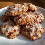 A close-up stack of delicious fruitcake cookies topped with a white glaze and colorful candied fruit pieces.