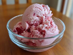 Two scoops of pink, swirled strawberry ice cream served in a clear glass bowl on a wooden table.