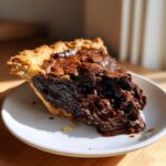 A slice of rich hot fudge pie with a gooey, melted chocolate center oozing onto a white plate.