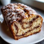 Close-up of a freshly baked apple bread loaf with a rich cinnamon swirl and white glaze drizzle.