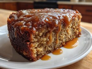 A close-up of a moist slice of apple dapple cake topped with a rich, dripping caramel sauce.
