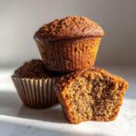 A stack of three moist bran muffins, with one cut in half showing the textured interior.