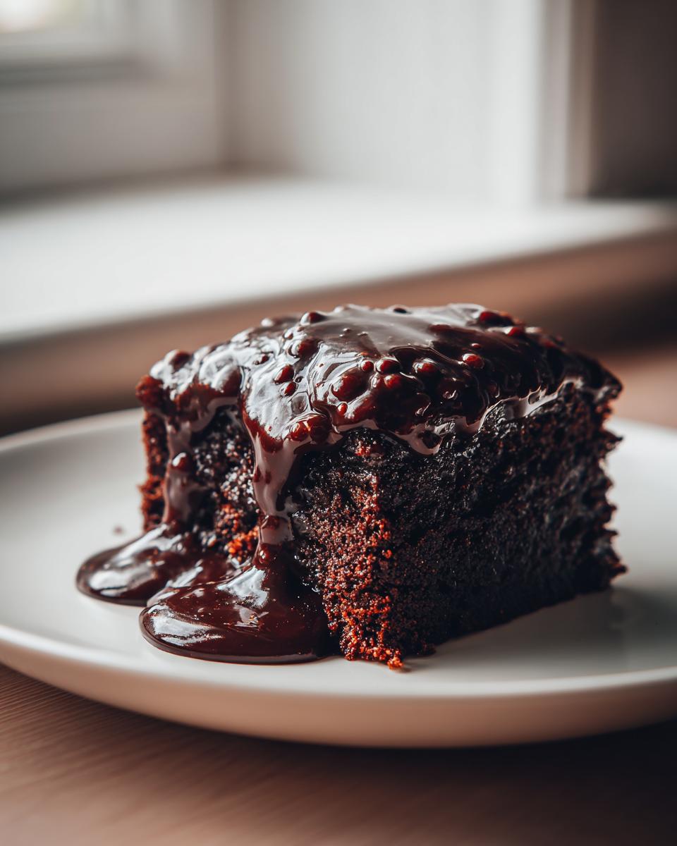 A rich, dark slice of chocolate pudding cake generously topped with glossy, warm chocolate sauce.