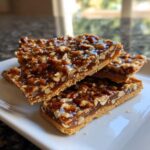 Three stacked bars of glossy pecan pie bark showing a thick layer of caramelized pecans over a shortbread crust.