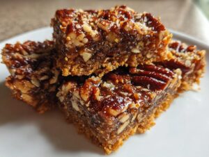 Close-up of stacked squares of glossy pecan pie bark showing a thick, gooey pecan topping over a crumbly crust.