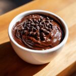 A close-up of rich, dark brownie batter dip in a white bowl, generously topped with mini chocolate chips.