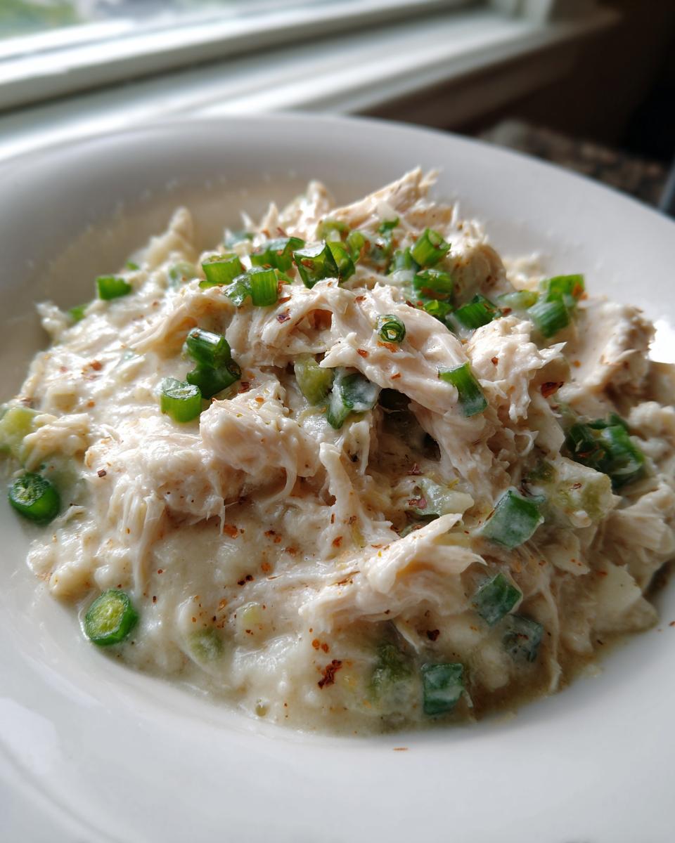 Close-up of shredded chicken mixed in a creamy sauce, topped with green onions, part of a cream cheese chicken chili recipe.