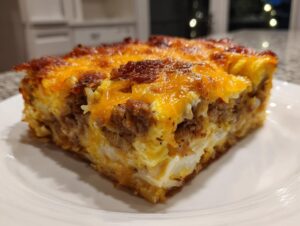 A close-up slice of a hearty christmas breakfast casserole with sausage, eggs, and melted cheddar cheese.