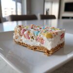 A slice of rich Christmas tree cheesecake featuring a graham cracker crust and colorful cereal pieces mixed into the filling.
