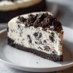 A perfect slice of creamy oreo cheesecake with a dark chocolate crust and topped with crushed oreo pieces.
