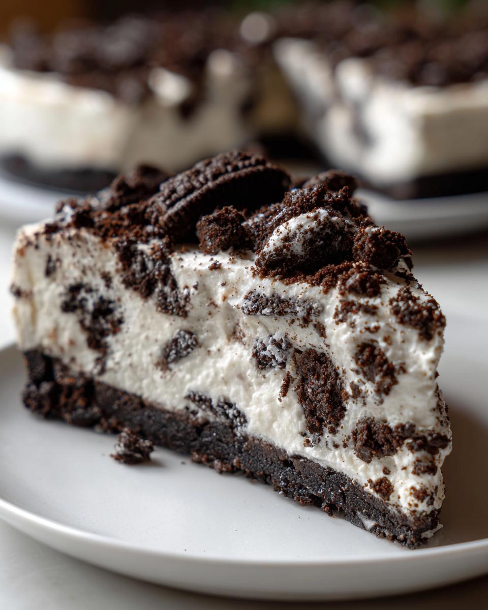 Close-up of a creamy slice of oreo cheesecake with a dark cookie crust and topped with crushed cookies.