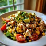 A vibrant bowl of southwest chicken salad featuring grilled chicken, corn, black beans, avocado, and creamy dressing.