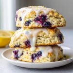 Three stacked lemon blueberry scones drizzled with white glaze and topped with lemon zest.