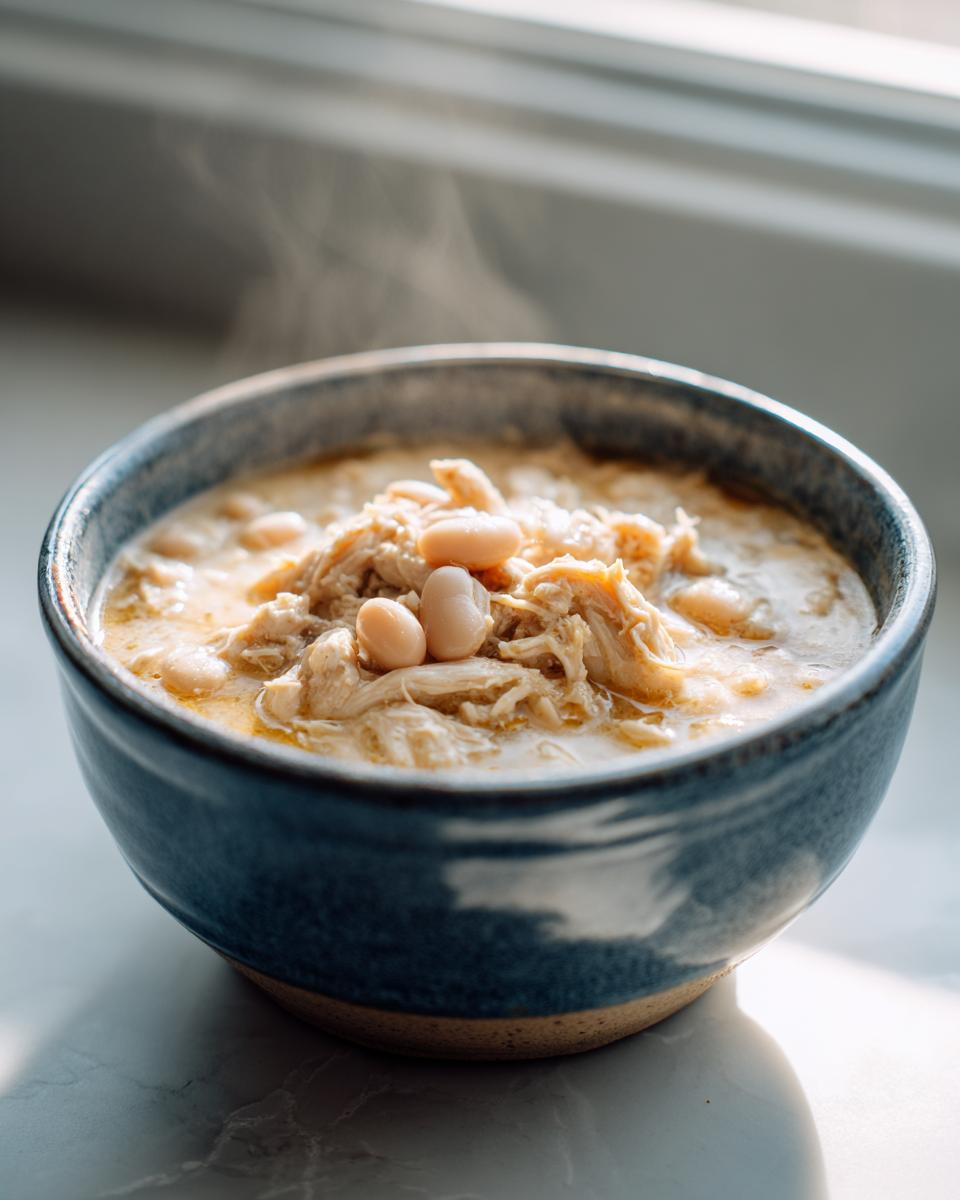 Close-up of steaming white chicken chili recipe with shredded chicken and white beans in a rustic blue bowl.