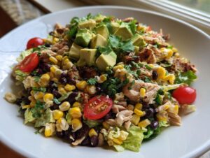 A vibrant bowl of southwest chicken salad featuring shredded chicken, black beans, corn, avocado, and cherry tomatoes.